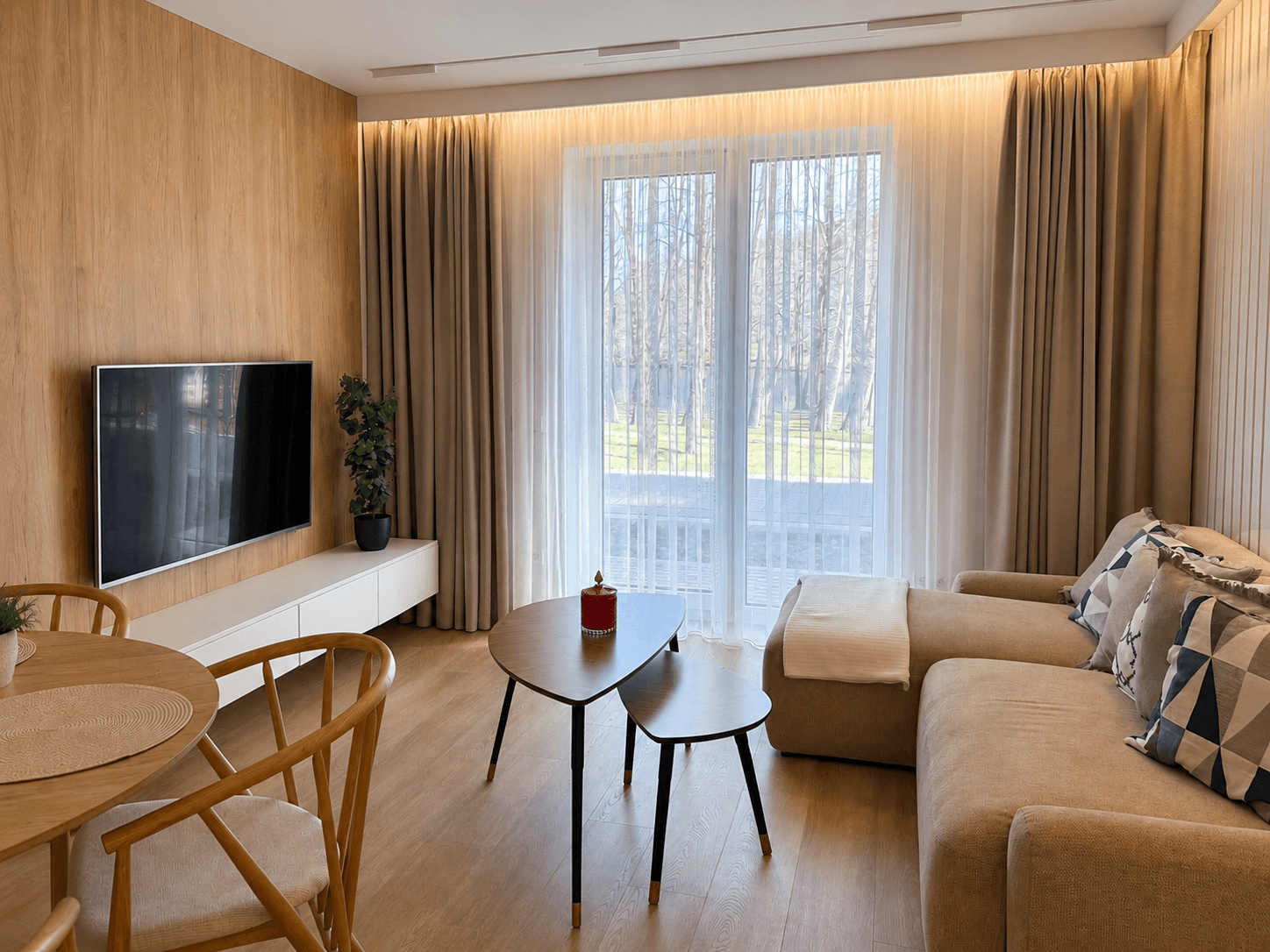 Jauki svetainės zona su sofa ir dideliu langu į mišką moderniuose apartamentuose